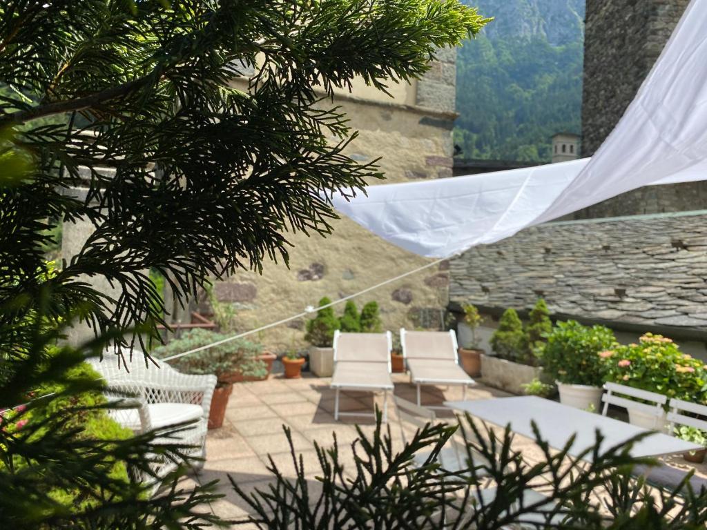 eine Terrasse mit weißen Stühlen, einem Tisch und einem Vorhang in der Unterkunft Dagli Olivari - Casa Dani in Gromo