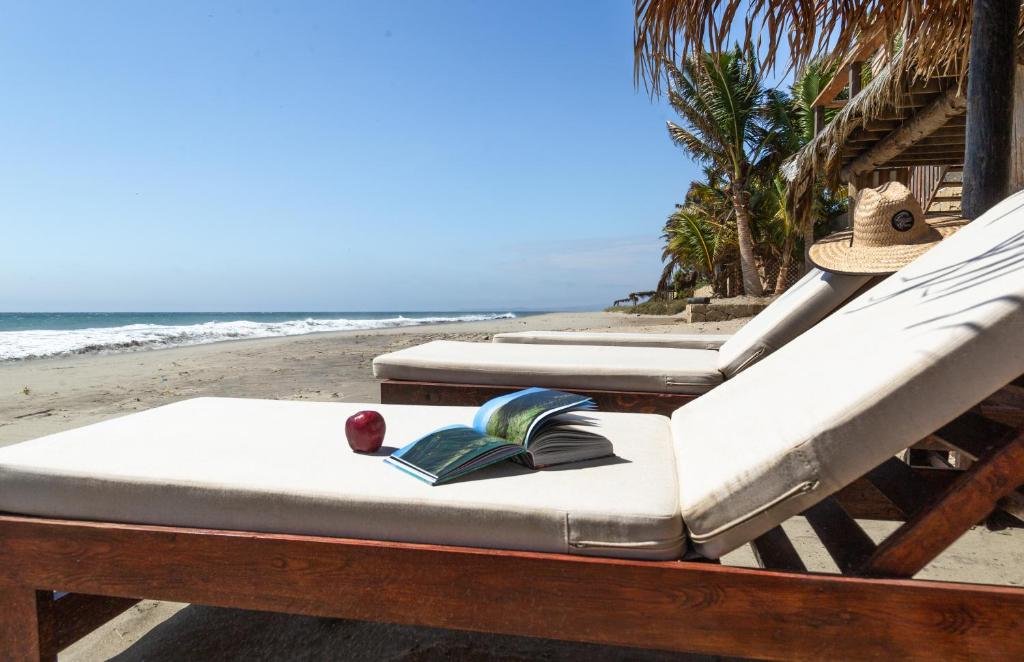 2 camas en una playa con un libro abierto y una manzana en Casa Punta Iguana Mancora, en Máncora