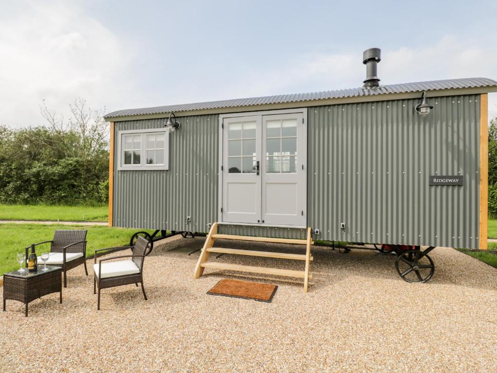 a green tiny house with a porch and chairs at Ridgeway in Faringdon