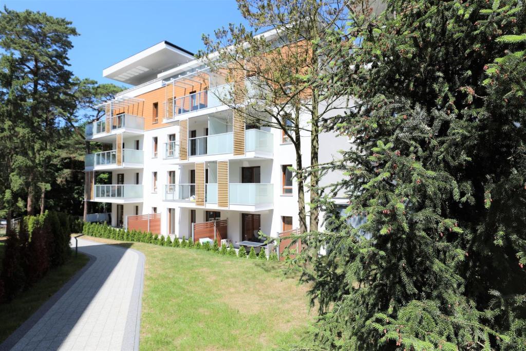 biały budynek apartamentowy z drzewami na pierwszym planie w obiekcie HoliApart in Nautikka Park w mieście Krynica Morska