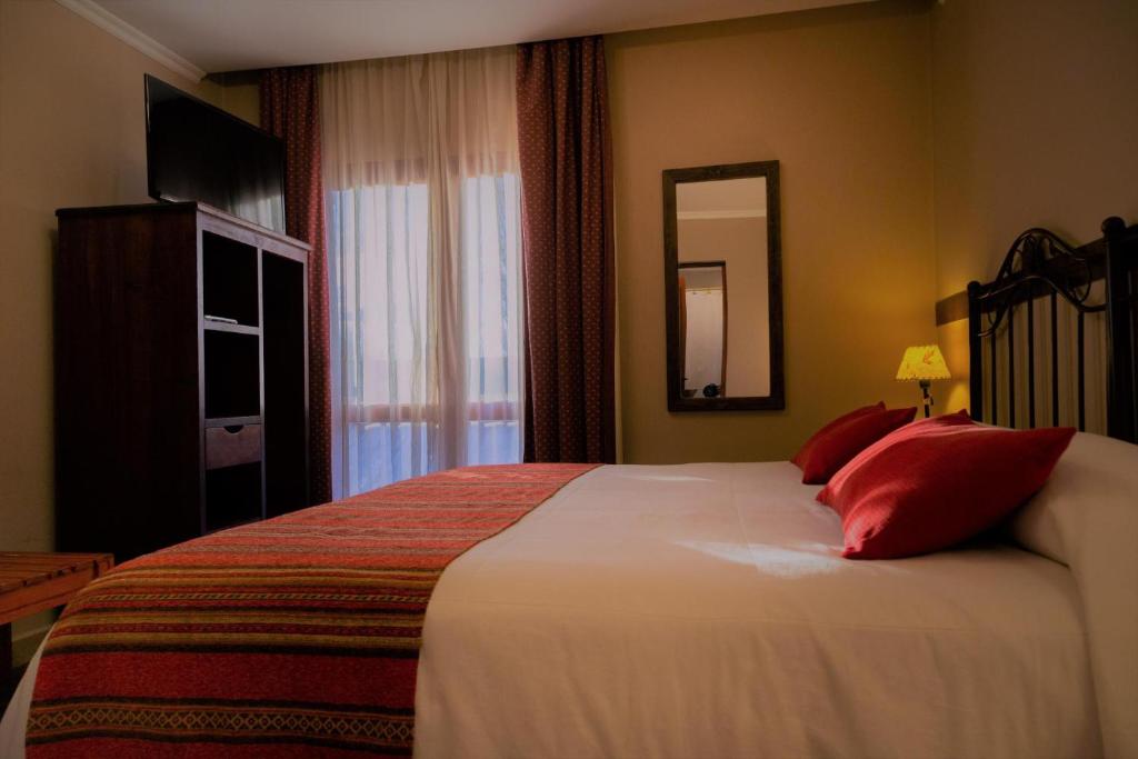 1 dormitorio con 1 cama grande con almohadas rojas y espejo en Don Pepe Hotel y Cabañas en El Calafate