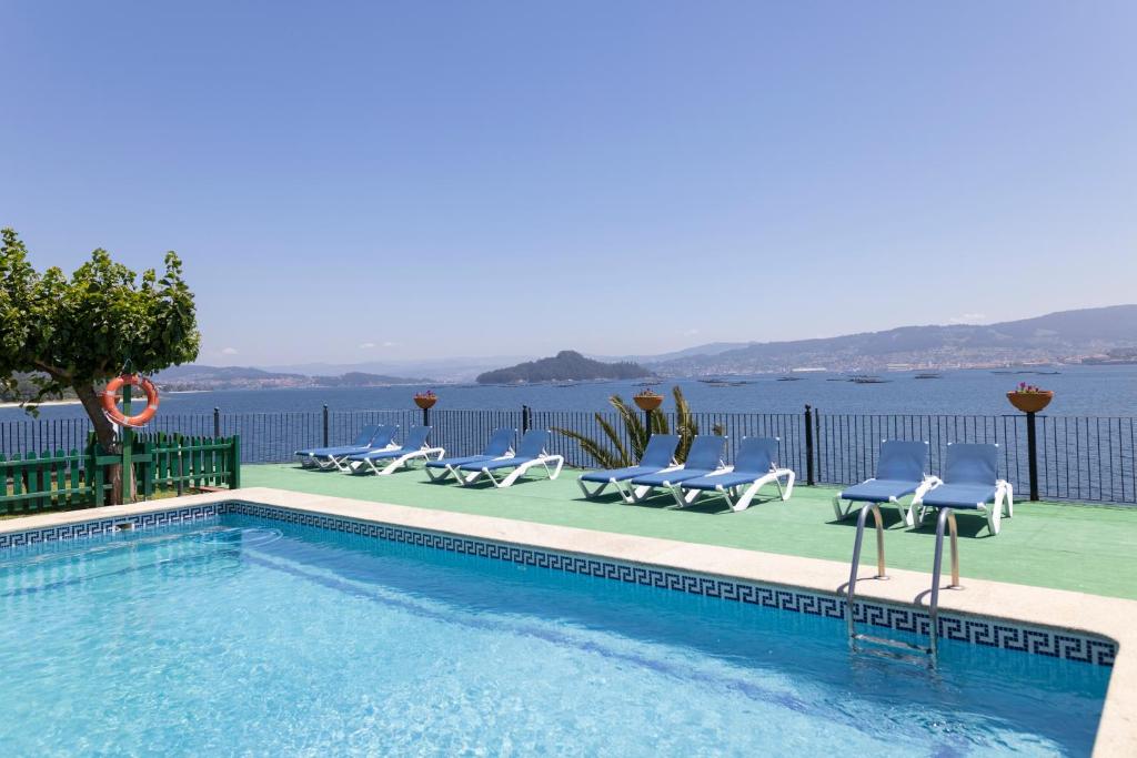 a swimming pool with chairs and a view of the water at Apartamentos Miramar Playa in Raxo