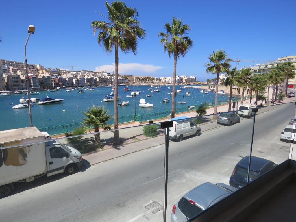 a street with cars parked next to a harbor with boats at Aquamarine Sea Front Apartments - First Floor in Marsaskala