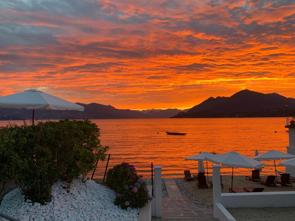 puesta de sol en una playa con mesas y sombrillas en Hotel La Sacca, en Stresa