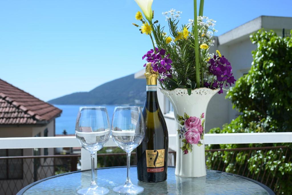 a bottle of wine and two glasses on a table with flowers at Aпартаменты Влаович in Igalo