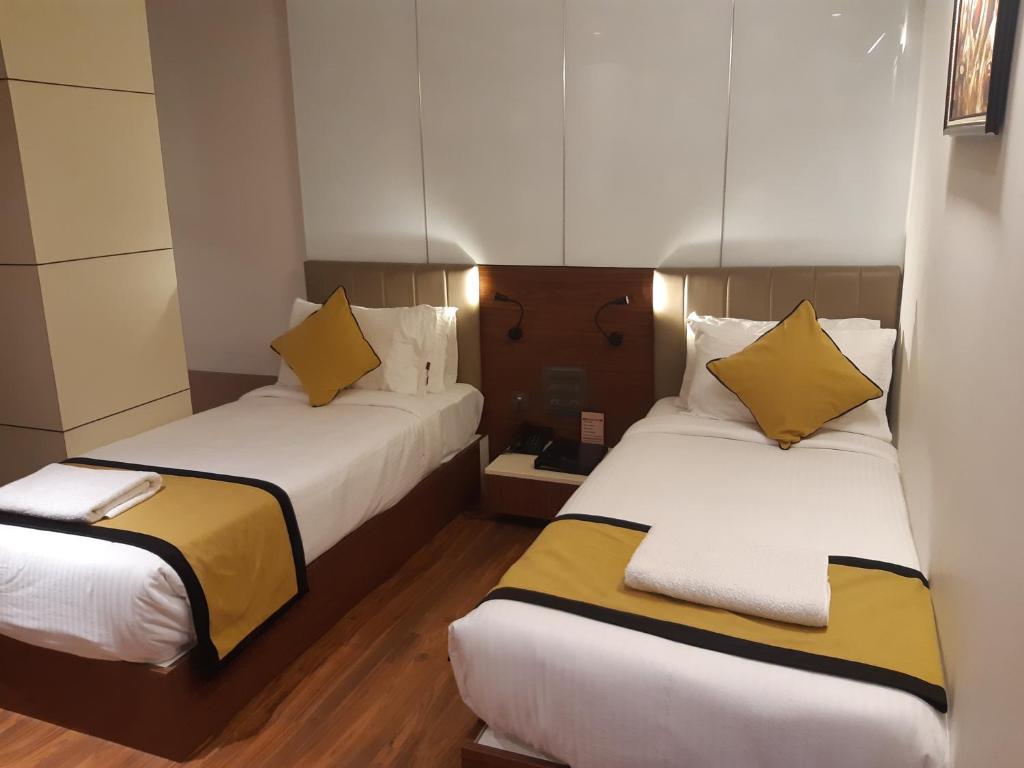 2 Betten in einem Hotelzimmer mit gelben Kissen in der Unterkunft Hotel Namo Residency in Vijayawāda