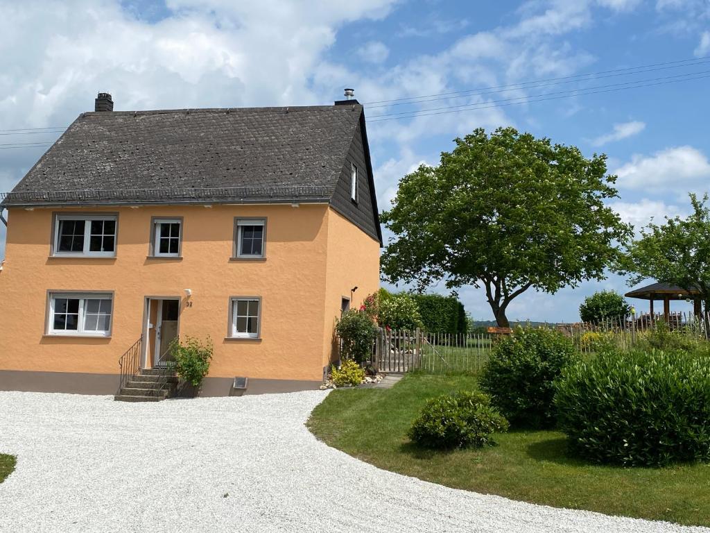 a yellow house with a tree and a gravel driveway at Ferienhaus Hunolstein in Morbach