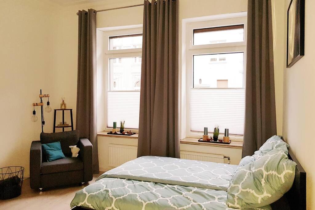 a bedroom with a bed and a chair and two windows at Apartment in Neudorf Nahe DU Zentrum und Uni/Zoo in Duisburg