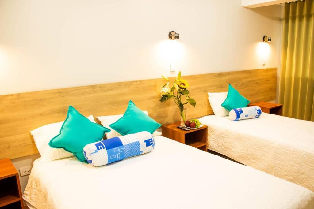 two beds in a hotel room with green and blue pillows at Casa Fideranda Apartments in Cusco
