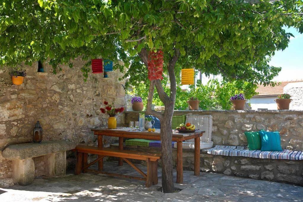 una mesa de madera bajo un árbol junto a una pared de piedra en Critamo cottage, en Gavalochori