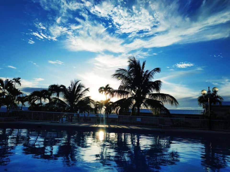 una piscina con palme e il tramonto sullo sfondo di LES EAUX BLEUES a Le Gosier