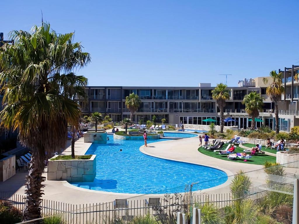a pool at a resort with palm trees and a building at Resort Apartment 109 in Torquay