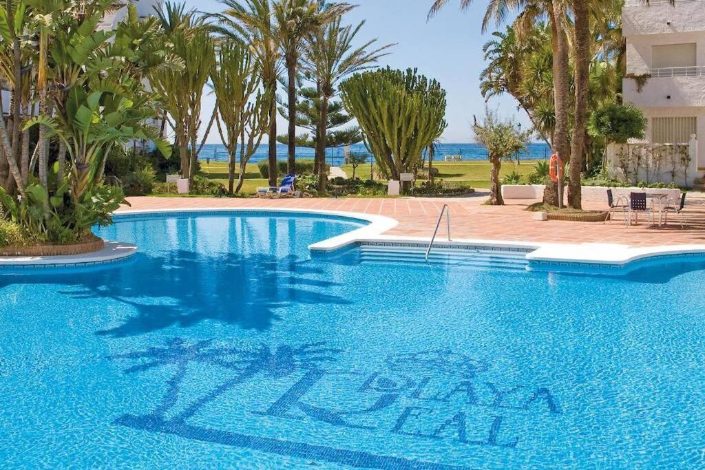 una piscina en un complejo con palmeras en Apartamento en Playa Real, en 1ª línea de playa, en Marbella