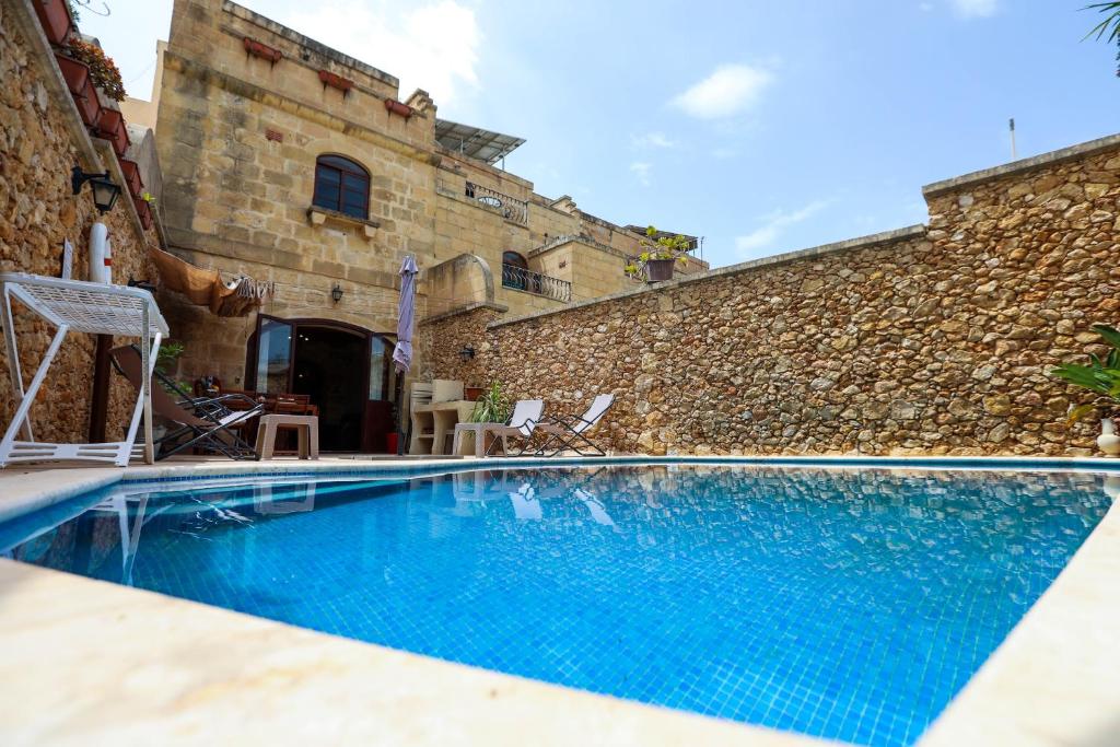 a swimming pool in front of a building with a stone wall at Ta'Ruzar Farmhouse in Xagħra