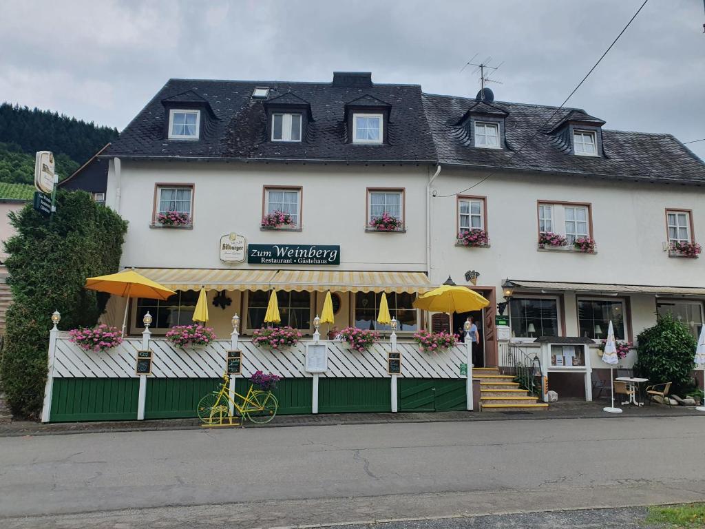 ein weißes Gebäude mit gelben Sonnenschirmen davor in der Unterkunft Gästehaus Hotel zum Weinberg in Burg (an der Mosel)