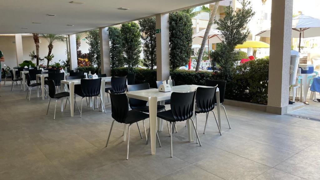 un restaurant avec des tables blanches et des chaises noires dans l'établissement Flat Prive das Thermas II - R3 Caldas, à Caldas Novas