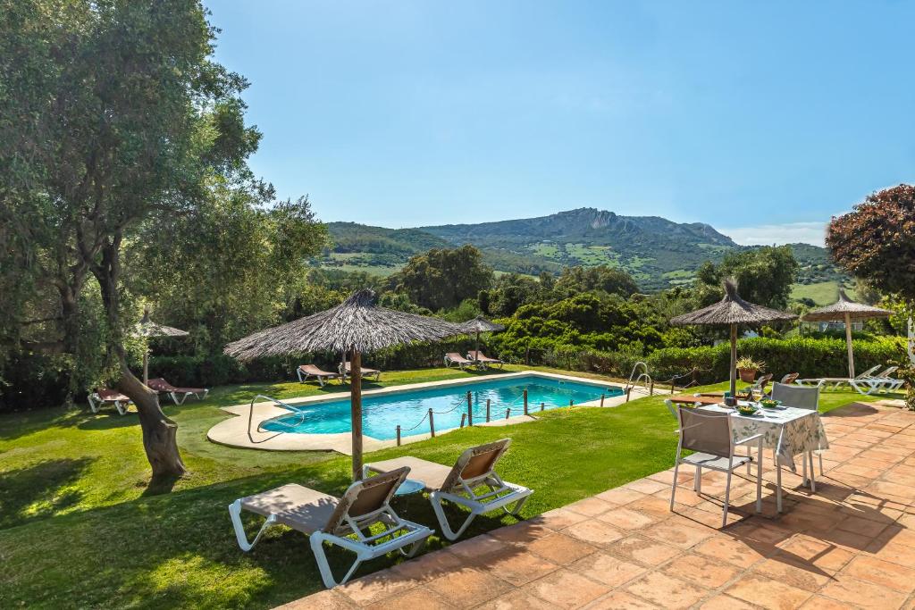 a swimming pool with two lawn chairs and an umbrella at Hotel-Apart CORTIJO LAS PIÑAS in Tarifa