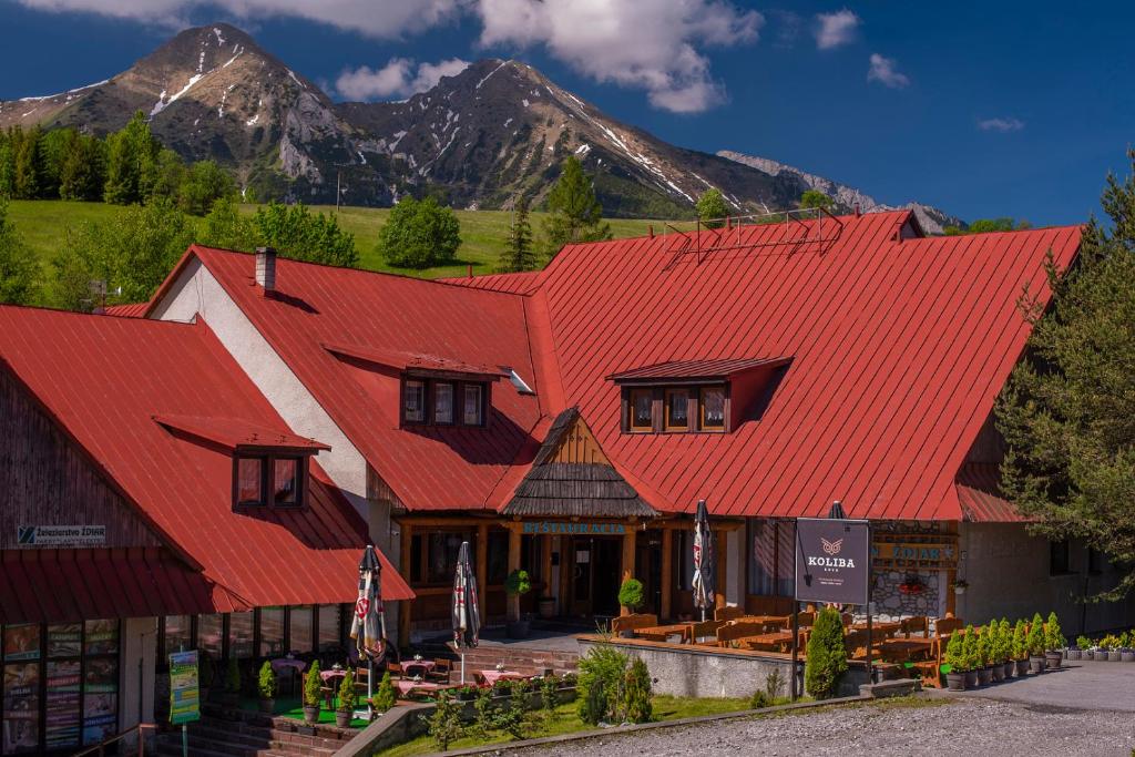 a building with a red roof with mountains in the background at Penzión Sova Ždiar in Ždiar