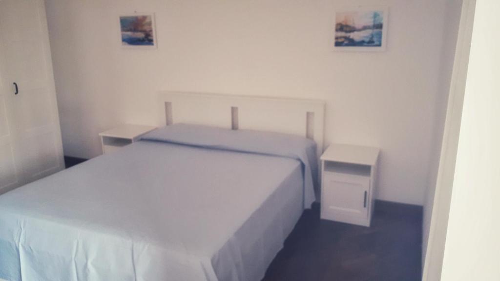 a white bedroom with a bed and a night stand at MAX and SUN parking privato nel prezzo in Sanremo