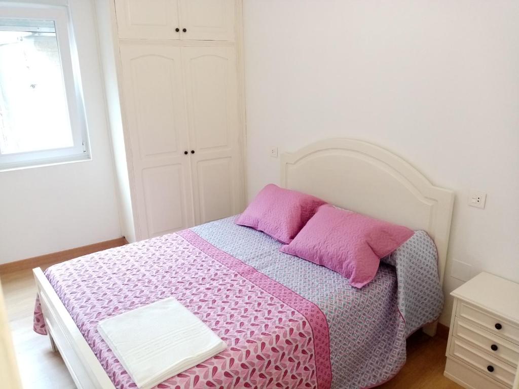 Habitación blanca con cama con almohadas rosas en Piso Muxía centro, en Muxía