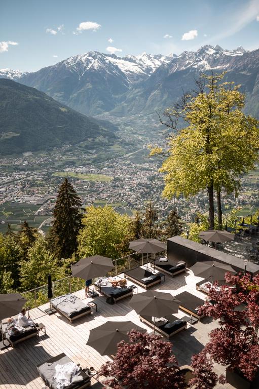 a patio with tables and umbrellas with mountains in the background at Miramonti Boutique Hotel in Avelengo