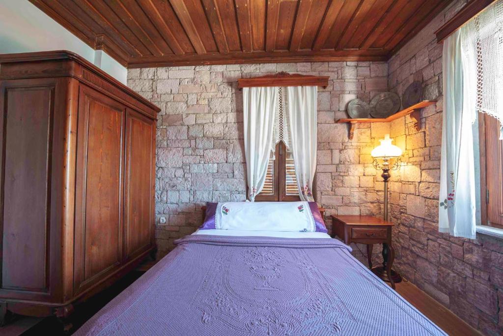1 dormitorio con cama morada en una pared de piedra en Cunda Tas Konak Otel, en Ayvalık