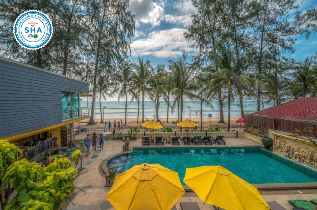 a resort pool with tables and umbrellas and the beach at Kamala Beachfront Apartment in Kamala Beach