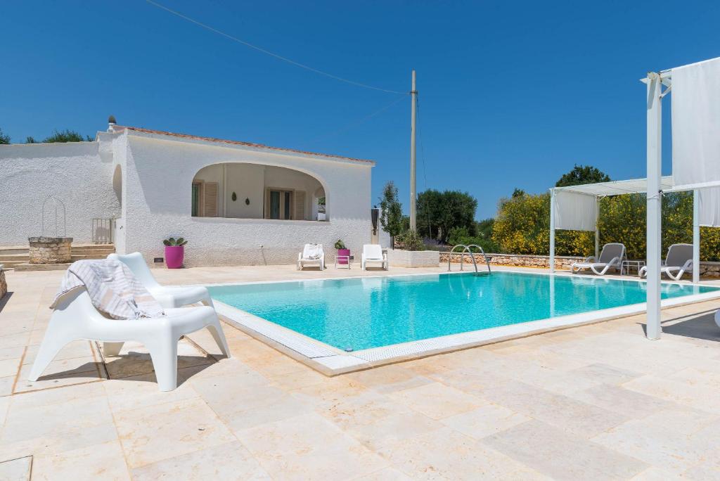 - une piscine avec une chaise blanche et une maison blanche dans l'établissement Charming Villas - Villa d'Itria with trullo, à Ostuni