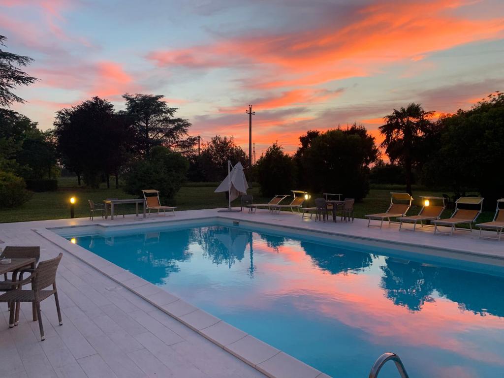 a swimming pool with chairs and a sunset in the background at Hotel Le Ville in Modena
