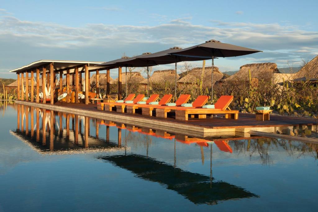 a dock with chairs and an umbrella on the water at Hotel Escondido, Puerto Escondido, a Member of Design Hotels - Adults Only in Puerto Escondido