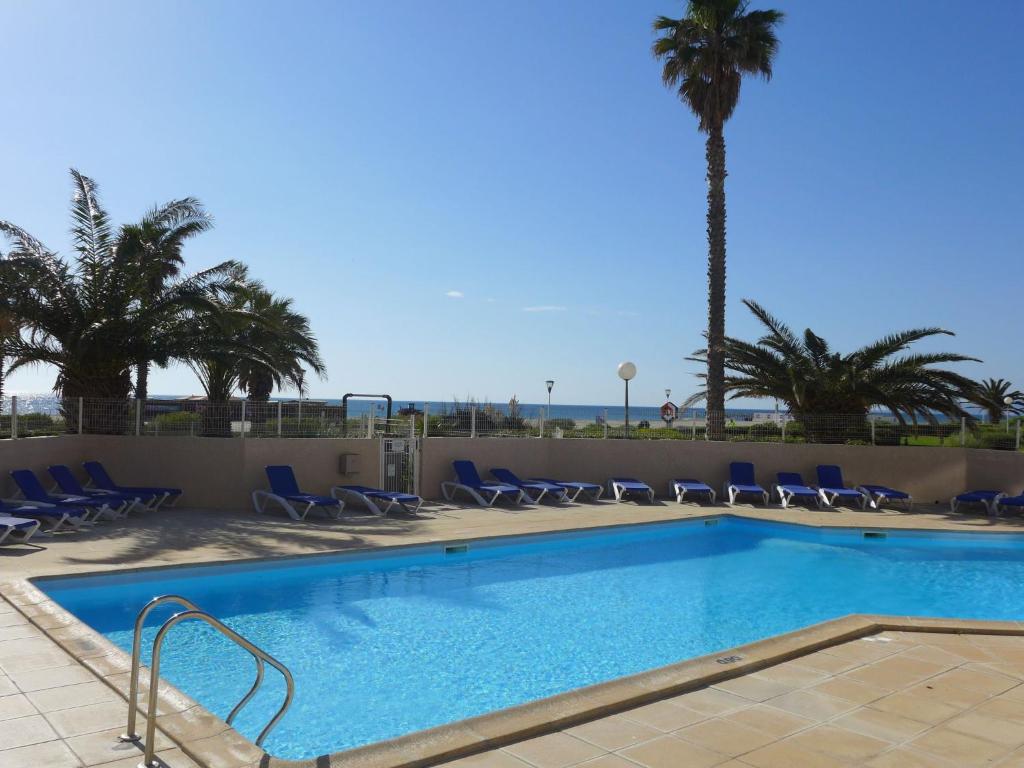 a swimming pool with chairs and a palm tree at Apartment Copacabana-21 by Interhome in Canet-en-Roussillon