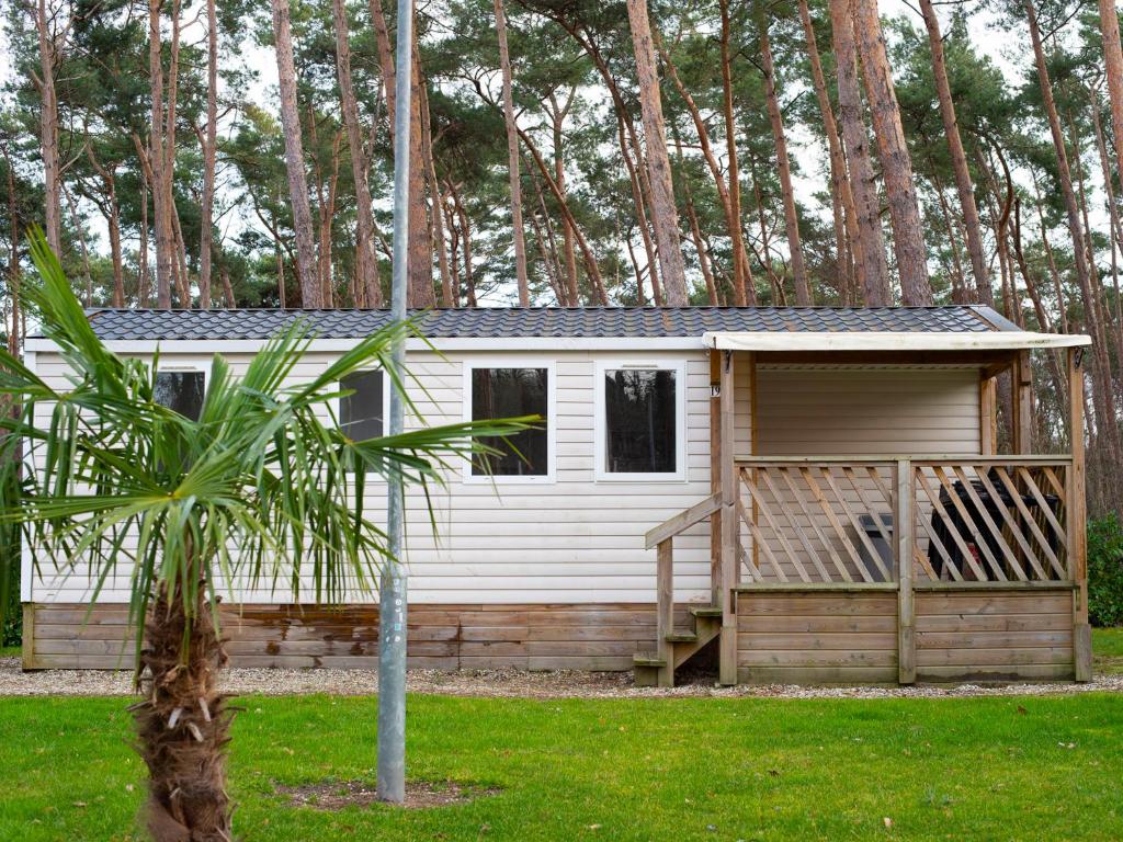 a small white cabin in a yard with trees at Holiday Home De Brenkberg-1 in Schinveld