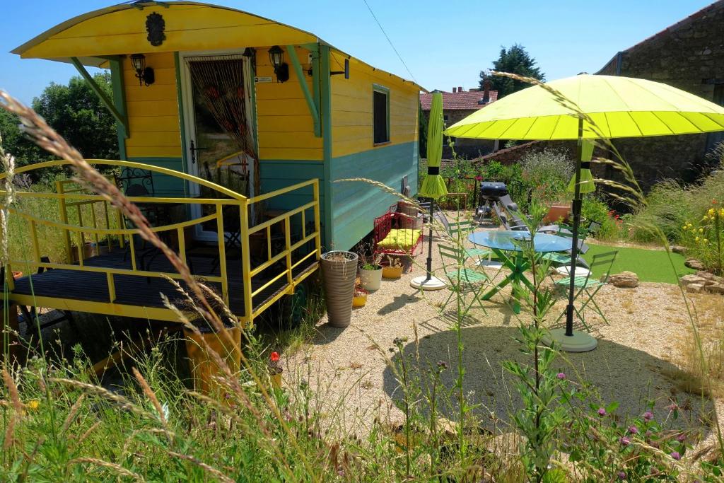 una casa amarilla con un paraguas amarillo en un patio en La Ferme De Chenevier, La Roulotte Fleurie 2/4pers, en Saint-Victor