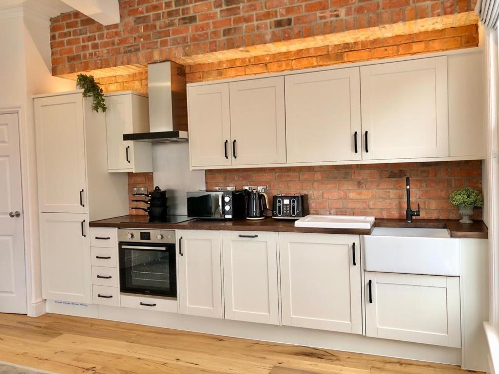 a kitchen with white cabinets and a brick wall at NG1 Lofts in Nottingham