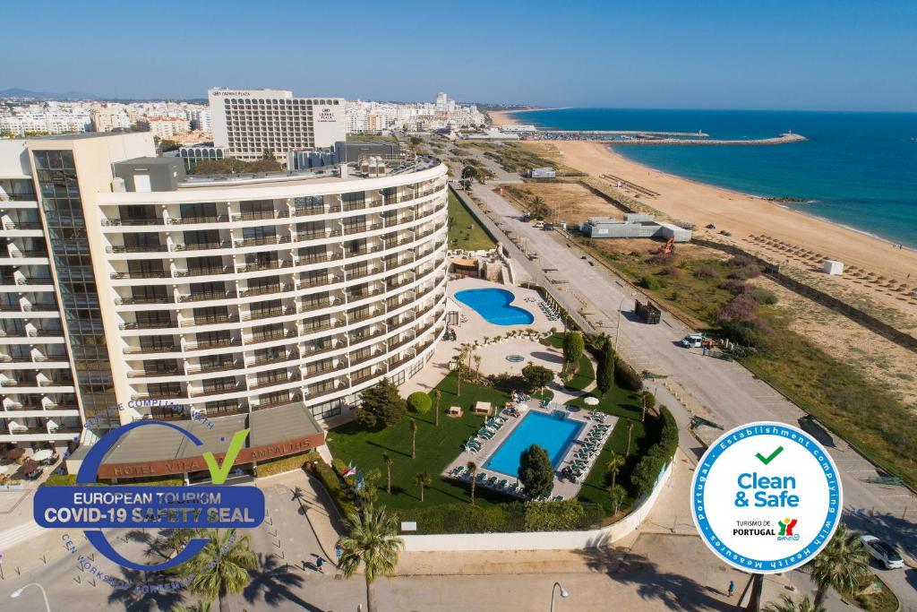 
a beach with a large building and some palm trees at Vila Gale Ampalius in Vilamoura

