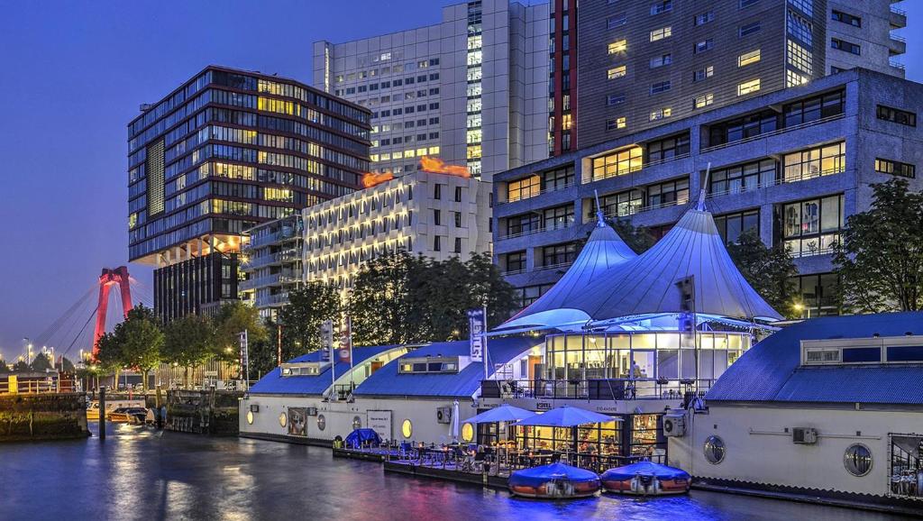 a building with blue roofs next to a river with buildings at H2OTEL Rotterdam in Rotterdam