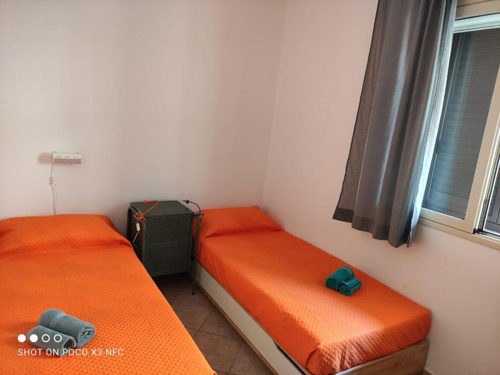 2 letti in una camera con lenzuola arancioni e finestra di La casa dei fico d'india a Marina di Ragusa