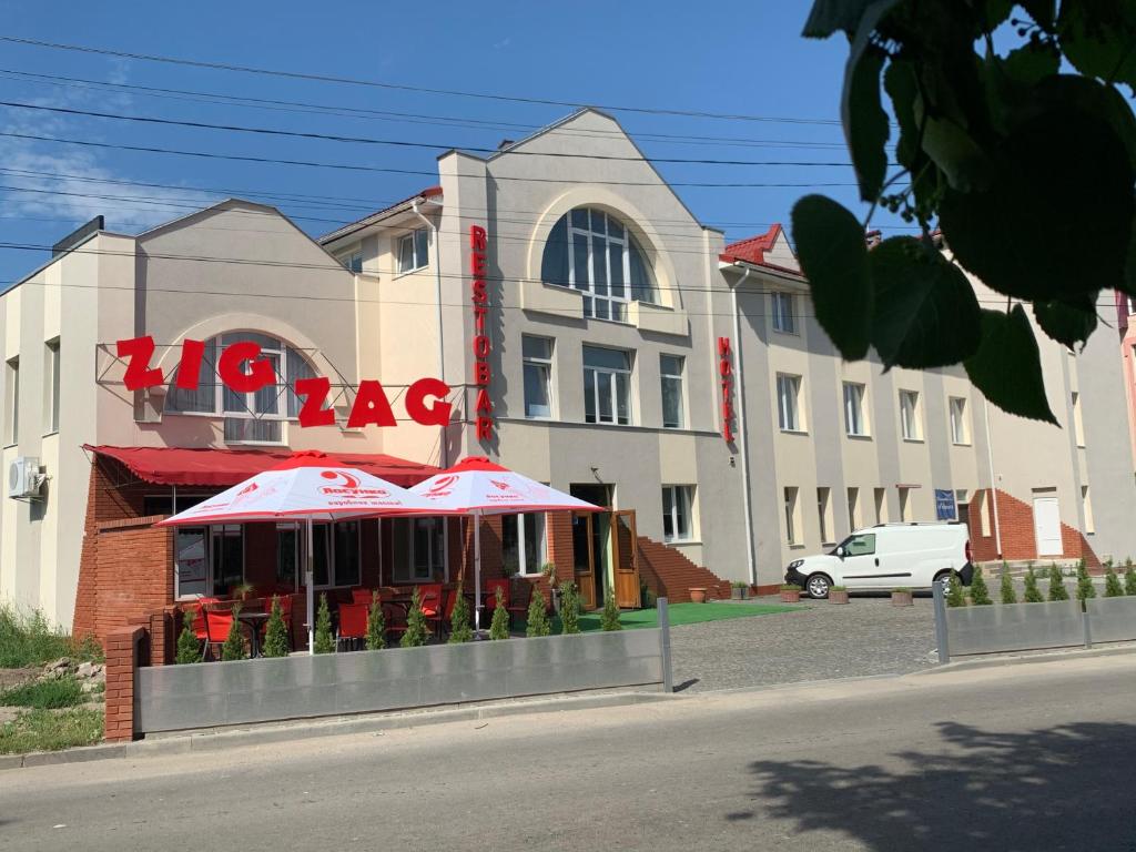 ein Gebäude mit einem Café mit roten Sonnenschirmen davor in der Unterkunft ZIG ZAG in Kamjanez-Podilskyj