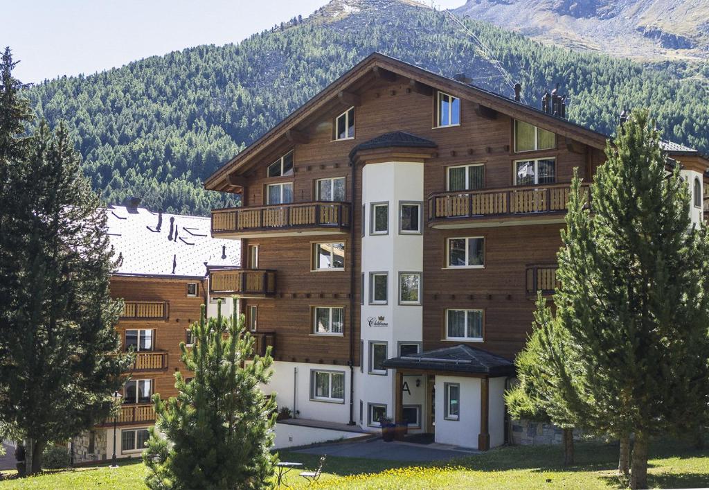 a large wooden building with trees in front of a mountain at Château A&B in Saas-Fee