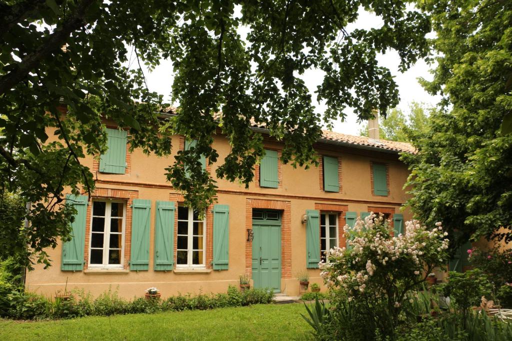 uma casa velha com persianas verdes e um quintal em La Closerie de l'Autan em Fenouillet