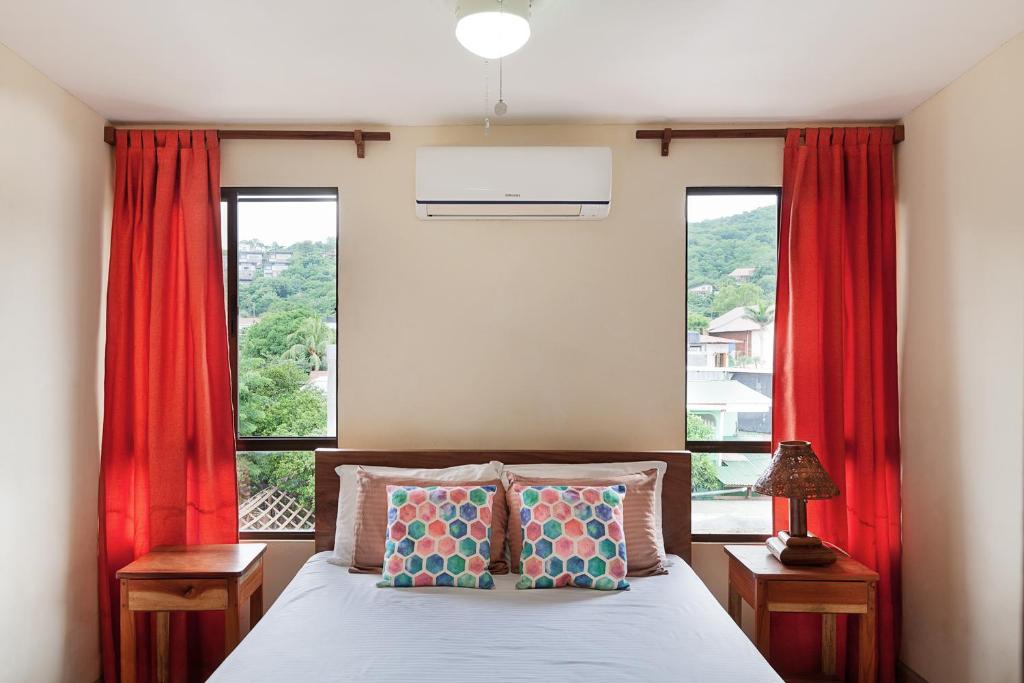 um quarto com uma cama e 2 janelas com cortinas vermelhas em Hostel Tropical and CoWorking em San Juan del Sur