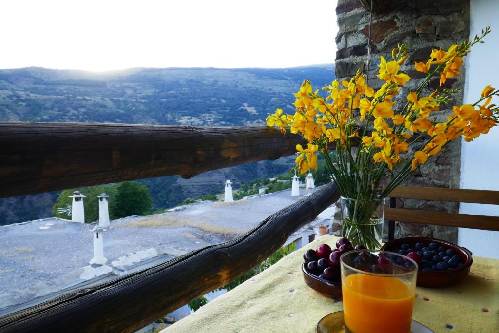 un jarrón de flores sobre una mesa con un vaso de zumo de naranja en La Higuera, en Bubión