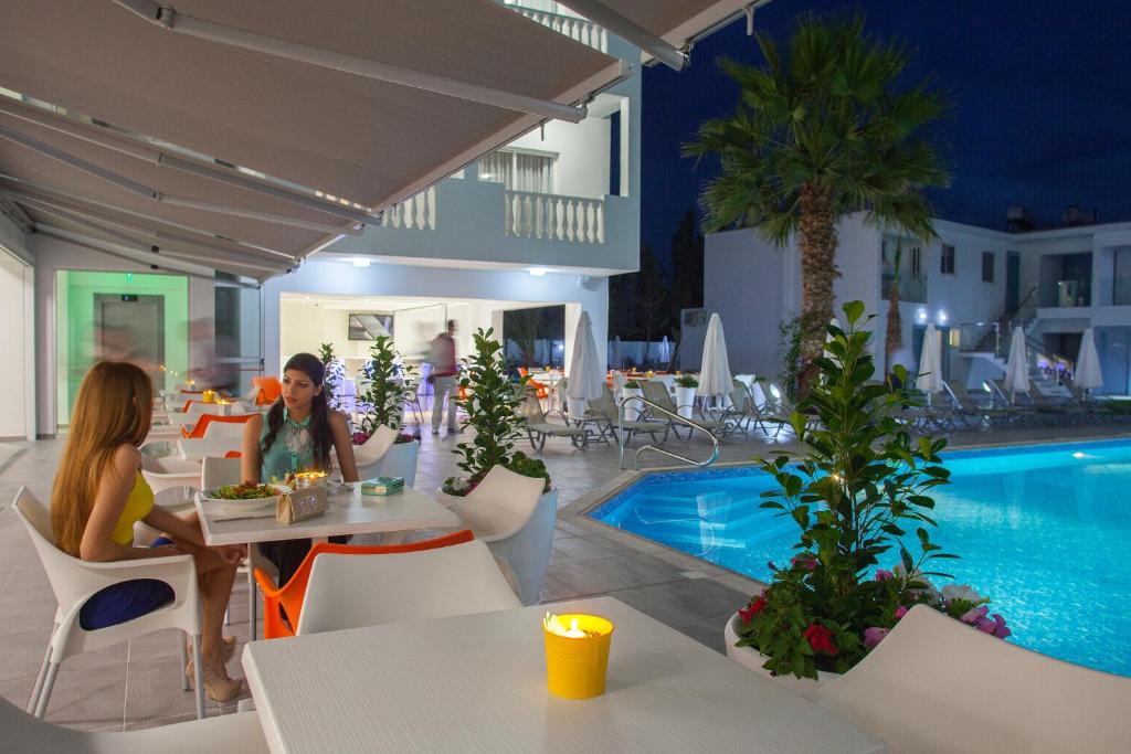 two women sitting at tables by a pool at a resort at Princessa Vera Hotel Apartments in Paphos