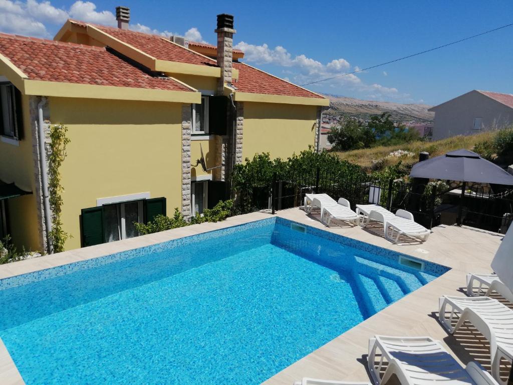 a swimming pool with chairs and a house at Family apartments Grguric in Pag