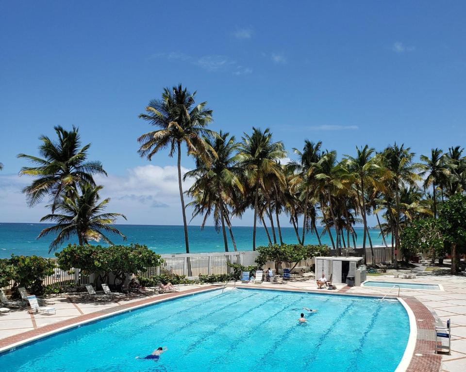 einen Pool mit Palmen und dem Meer in der Unterkunft KASA Ocean Breeze - Cabana Studio Apartment BEACHFRONT CONDO POOL in San Juan