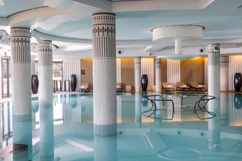 a swimming pool with columns and chairs in a building at Thalazur Saint Jean de Luz - Hôtel & Spa in Saint-Jean-de-Luz