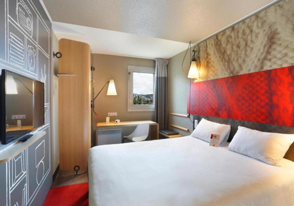 une chambre d'hôtel avec un grand lit et un bureau dans l'établissement Ibis Le Havre Sud Harfleur, à Harfleur