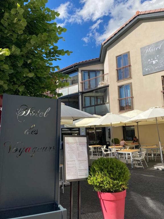 un panneau devant un hôtel avec des tables et des parasols dans l'établissement Logis Hotel Restaurant des Voyageurs, au Malzieu-Ville