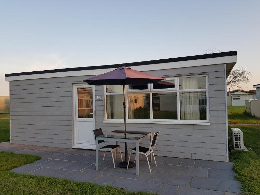 a table with an umbrella in front of a shed at Camber Sands Holiday Chalets - The Grey in Camber