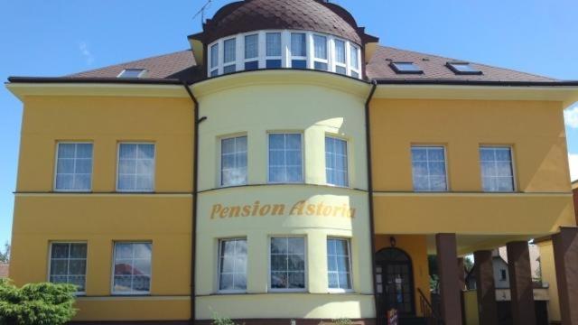 un bâtiment jaune et blanc avec un panneau représentant la vengeance dans l'établissement Pension ASTORIA, à Klášterec nad Ohří